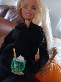 a barbie doll sitting on a couch with a drink in her hand and an orange pumpkin behind her