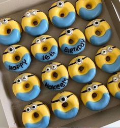 twelve yellow and blue decorated donuts in a box with happy birthday written on them