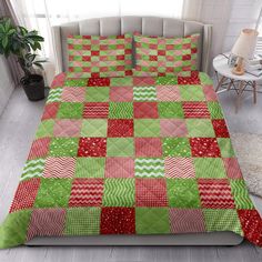 a bed covered in a green and red quilt next to a white table with a potted plant