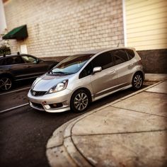 a silver car parked on the side of a road next to a brick building and another black car