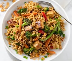 a white plate topped with noodles and veggies next to a fork on top of a table