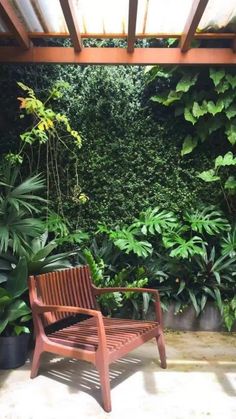 a wooden bench sitting in front of a lush green plant covered wall on the side of a building