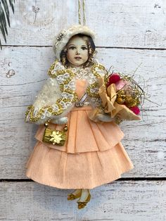 an ornament hanging on the side of a wooden wall with a doll holding flowers