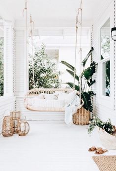 the front porch is decorated with hanging plants and wicker hammock chairs for seating