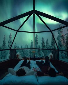 two people laying on a bed in front of an aurora bore viewing platform at night