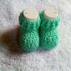 a pair of green crocheted slippers sitting on top of a white rug