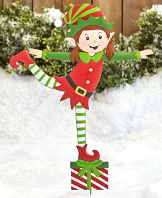 a christmas elf standing on top of a box in the snow with his arms out