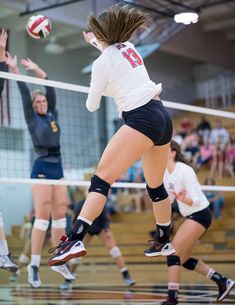 a volleyball player jumping up to hit the ball with her racket while other players look on