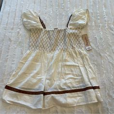 a white dress with brown trims is laying on a bed and has a tag attached to it