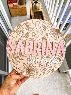 someone holding up a wooden sign that says sabrana with flowers on the front