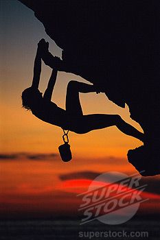 a man climbing up the side of a cliff at sunset with his hands in the air