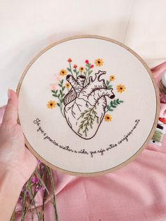 someone is holding a cross stitch heart with flowers on it