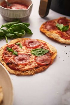 three small pizzas with pepperoni and spinach leaves on the table next to some dipping sauce