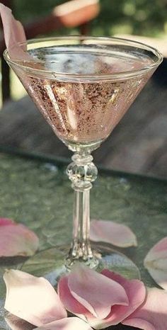 a glass filled with liquid sitting on top of a table next to pink flower petals