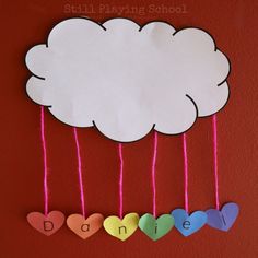 a paper cloud hanging from strings with name puzzle on it and hearts attached to the string