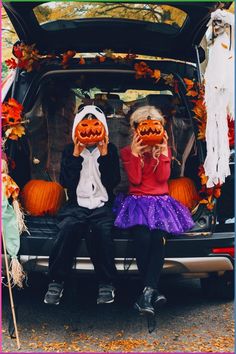 two children sitting in the back of a car with pumpkins on their faces and hands