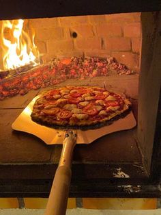 a pizza sitting on top of a wooden spatula in front of an open fire