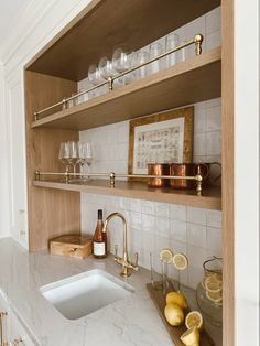 a kitchen with marble counter tops and wooden shelves filled with glasses, lemons, and wine bottles