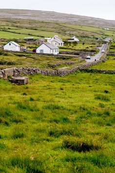 a grassy field with houses on the side and green grass growing in front of it