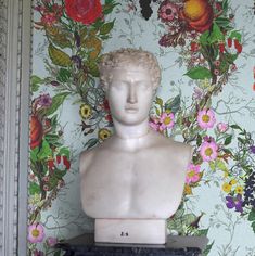 a bust of a man with flowers on the wall behind it