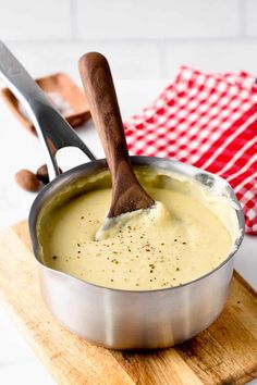 a wooden spoon in a pan filled with cheese sauce on a cutting board next to a red and white checkered napkin