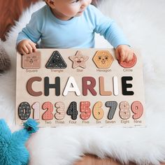 a baby holding up a wooden sign with numbers and shapes