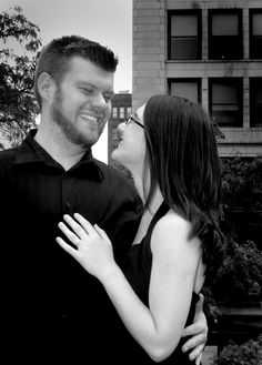 black and white photograph of a man and woman smiling at each other in front of tall buildings