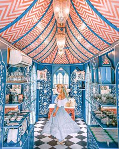 a woman in a blue and white dress standing inside of a room filled with shelves