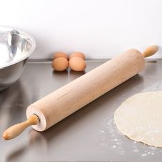 an uncooked pizza dough and rolling pin on a metal countertop next to a bowl with three eggs