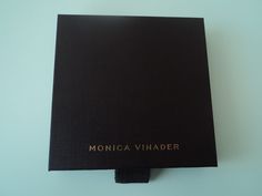 a black book sitting on top of a white table next to a blue wall with the words monica vinader written on it