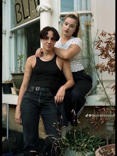 two women are sitting on the ledge of a building and one is holding her arm around the other woman's shoulder