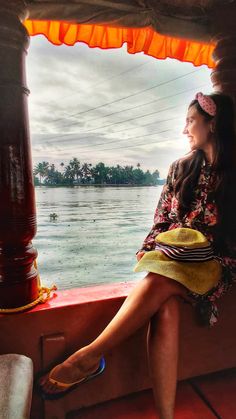 a woman sitting on the edge of a boat looking out at water and land below