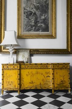 a painting hangs on the wall next to a yellow cabinet with two drawers and a lamp