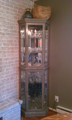 a tall china cabinet with wine glasses on top in front of a brick fire place