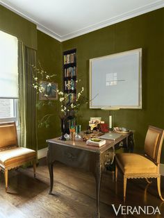 a living room with green walls and wooden flooring, two chairs in front of the table