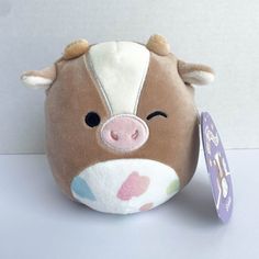 a small stuffed animal with a tag on it's ear, sitting next to a white wall