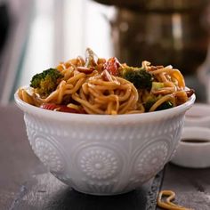 a white bowl filled with noodles and broccoli on top of a wooden table