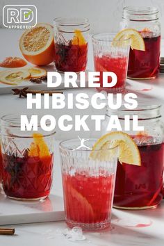 four glasses filled with red liquid and orange slices on top of a table next to some other