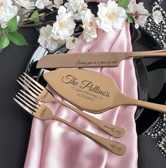 three forks and two spoons sitting on top of a pink table cloth next to flowers