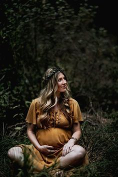 a pregnant woman sitting in the grass with her hands on her stomach and looking off into the distance