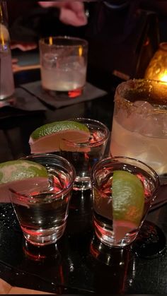 three glasses filled with different kinds of drinks on top of a black table next to a candle