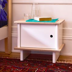 a small table with a book and some glasses on it in front of a bed