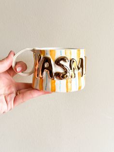 a hand holding a coffee mug with the word asm painted on it