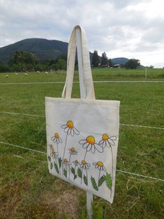 a white bag with daisies painted on it sitting in the grass near a fence