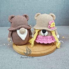 two crocheted teddy bears wearing hats on top of a wooden board with string