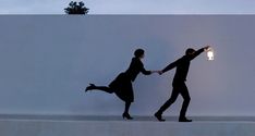 two people holding hands while standing in front of a wall with a light on it