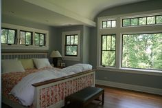 a large bed sitting in the middle of a bedroom next to two windows with lots of natural light