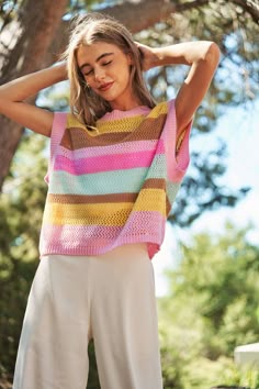 a woman standing in front of a tree wearing a multicolored knitted sweater