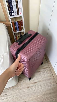 a person holding onto a pink suitcase in front of a book shelf with books on it