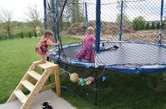 two young children playing on a trampoline in the yard, with one child climbing up to the trampoline